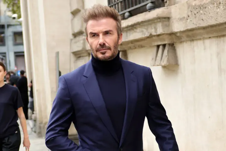 David Beckham luce un elegante traje azul con jersey de cuello alto, caminando con confianza.