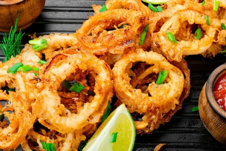 Aros de calamar rebozados y fritos, servidos con limón y salsa de tomate. Ideales para recetas con calamares.