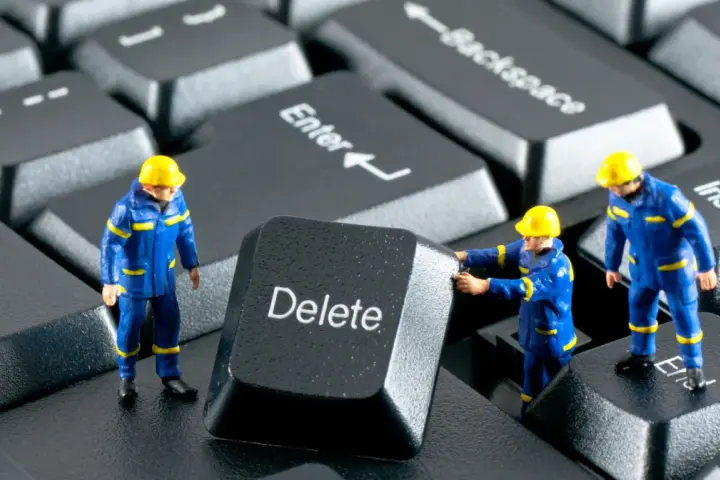 Figurki robotników w niebieskich kombinezonach próbują usunąć klawisz "Delete" z klawiatury. Działają jak incogni, usuwając niechciane dane.