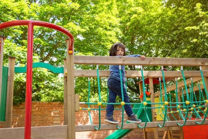 Chłopiec na placu zabaw, wesoły park rysunek. Dziecko wspina się po drewnianej konstrukcji z zielonymi linami.