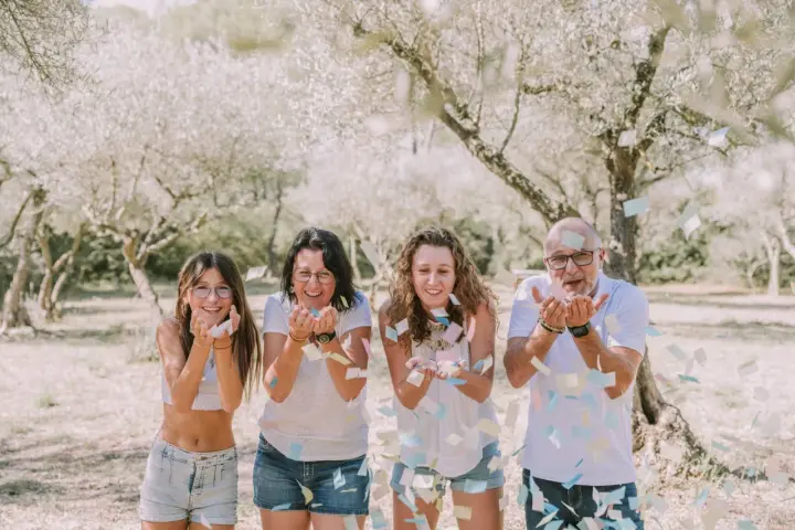 Photographie lifestyle : une famille lance des confettis sous des arbres fleuris, un moment de joie capturé.