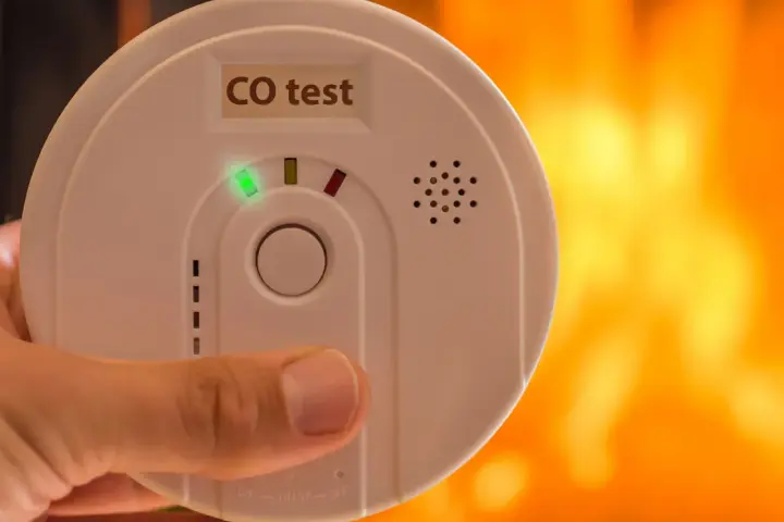 Detektor czadu z zieloną diodą i napisem "CO test" na tle płomieni.