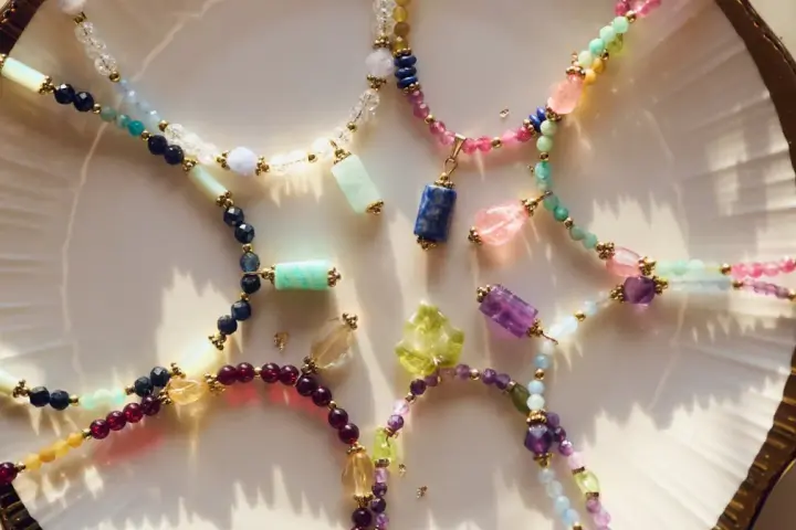 Kolorowe naszyjniki z kamieni szlachetnych, w tym lapis lazuli znak zodiaku, ułożone na talerzu.