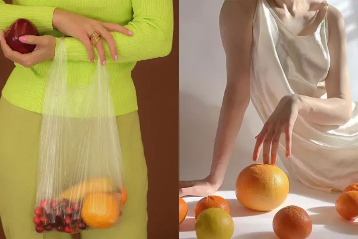 Mani che tengono una mela e una busta con ciliegie e arance. Altre arance e un limone sparsi su uno sfondo chiaro, evocando un'essenza di fruit extract.