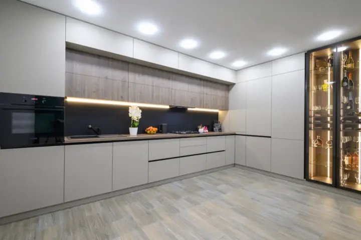 Cocina moderna con armarios grises y vitrina iluminada. El suelo de madera clara es perfecto para suelos para cocinas sin obras, aportando calidez y estilo.