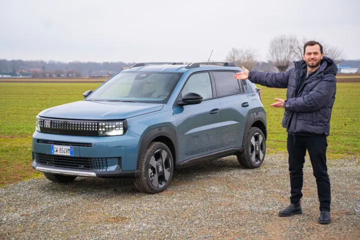 Mężczyzna prezentuje nowy, niebieski Fiat Grande Panda na tle zielonego pola.