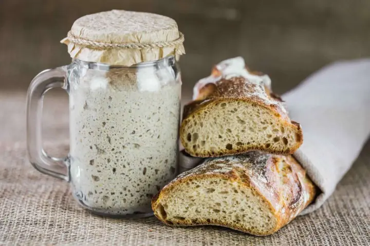 Un barattolo di rinfresco lievito madre accanto a fette di pane rustico.