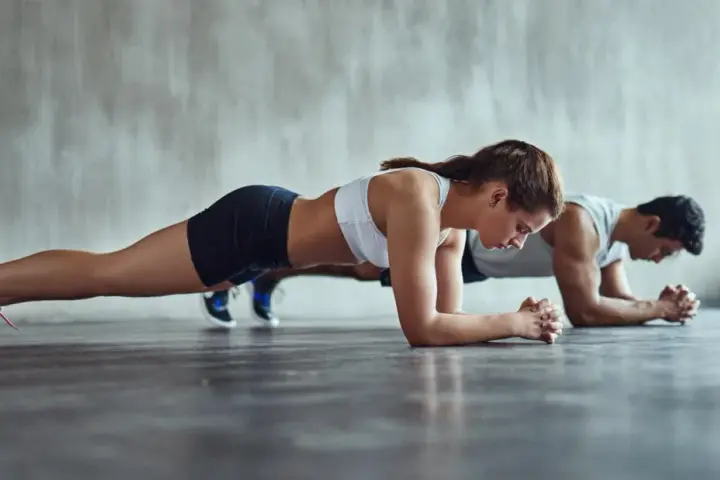 Un couple concentré fait la planche côte à côte dans une salle de sport.