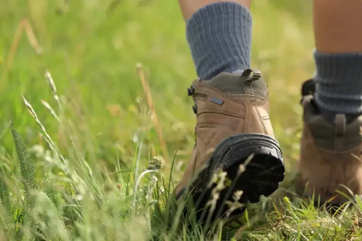 Wanderstiefel mit grauen Socken, die durch hohes Gras treten. Die richtigen Socken sind entscheidend, welche Socken zum Wandern am besten geeignet sind.