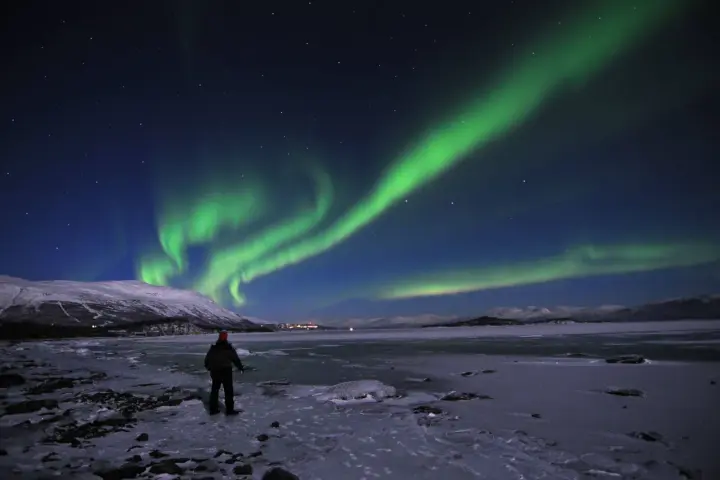En ensam person står på en isig strand och ser på det magiska abisko norrsken som dansar över himlen.