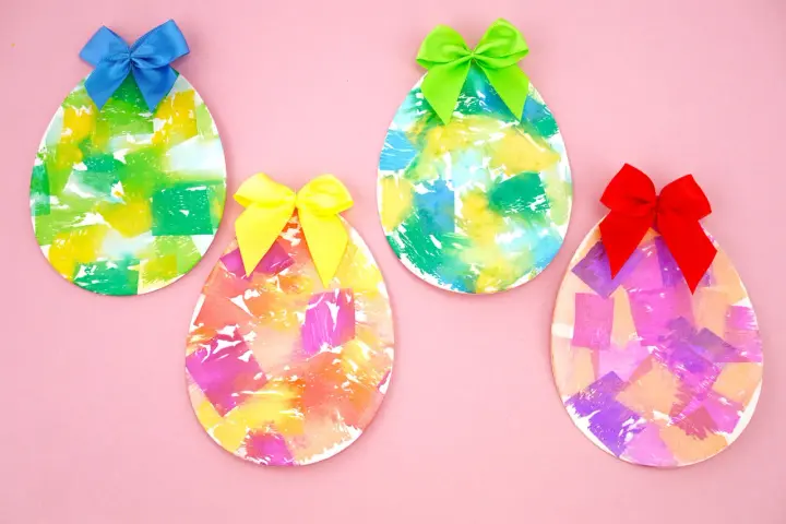 Quatre œufs décorés de papier crépon coloré et ornés de rubans sur fond rose.