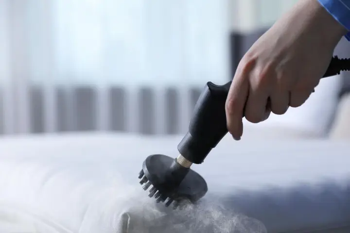 Main d'une personne utilisant un nettoyeur vapeur pour nettoyer un matelas en mousse. Une méthode efficace pour savoir comment nettoyer un matelas en mousse.