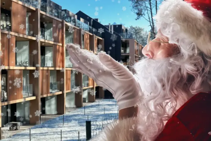 Śnieżynki tańczą wokół Świętego Mikołaja dmuchającego śniegiem na nowoczesny hotel. Czas na mikołajki w hotelu!