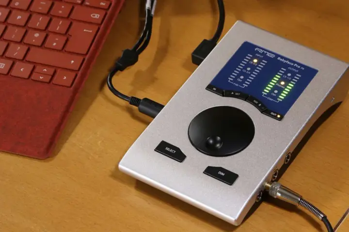 Srebrny interfejs audio RME Babyface Pro FS podłączony do czerwonej klawiatury. Idealny do mobilnego studia.