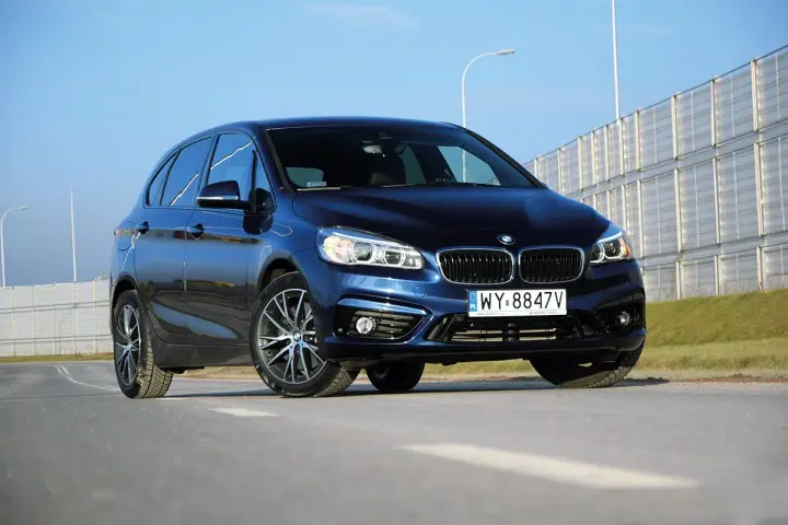 Ciemnoniebieski BMW van na tle jasnego nieba i barier dźwiękochłonnych.