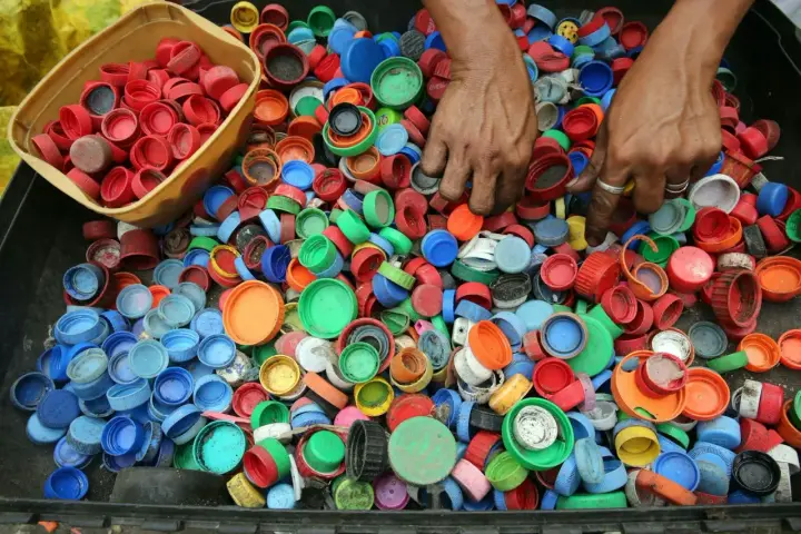 Ręce zbierają kolorowe nakrętki, pokazując, dlaczego zbiera się nakrętki – dla recyklingu i pomocy potrzebującym.
