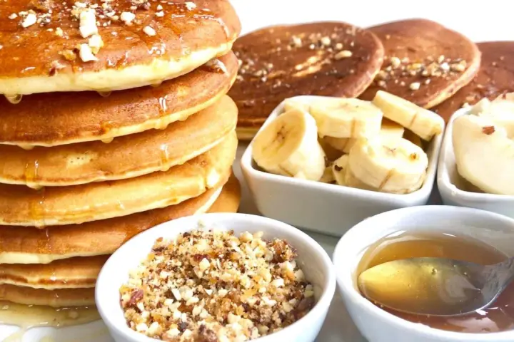 Pile de pancakes dorés arrosés de miel, accompagnés de rondelles de banane, de noix concassées et d'une cuillère de miel. Un délice pour le petit-déjeuner !