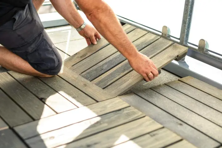Un homme installe des dalles de terrasse en bois sur son balcon. Une belle idée sol balcon pour un espace extérieur accueillant.