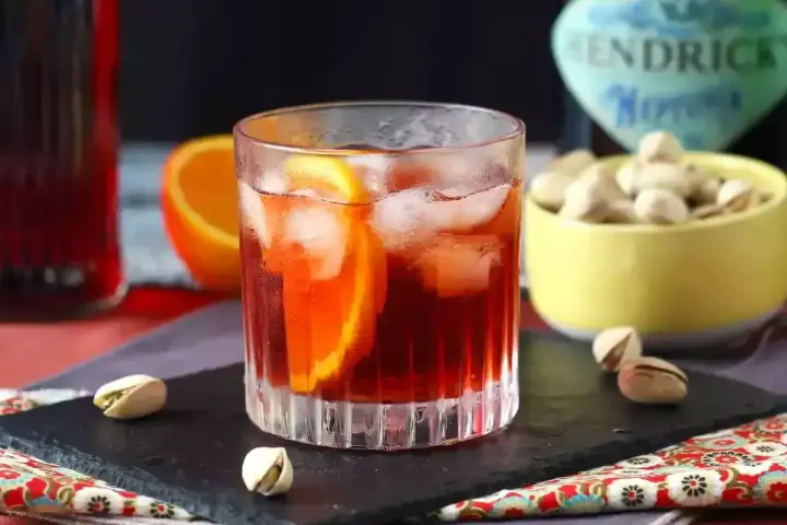 Przepis na Negroni Sbagliato: orzeźwiający drink z pomarańczą i lodem, obok miseczka pistacji.