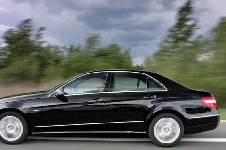 Czarny Mercedes E350 pędzi po drodze, mijając rozmyte zielone drzewa.