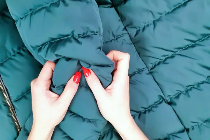 Manos con uñas rojas arrugan una chaqueta verde oscuro. ¡Por fin he lavado un plumas en la lavadora y está como nuevo!