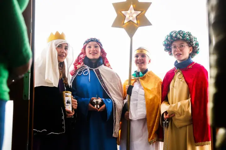Vier Kinder als Sternsinger evangelisch verkleidet, mit Stern und Spendenbüchse, stehen vor einer Tür.