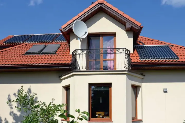 Elegancki wykusz w domu z balkonem i anteną satelitarną. Na dachu widoczne kolektory słoneczne.