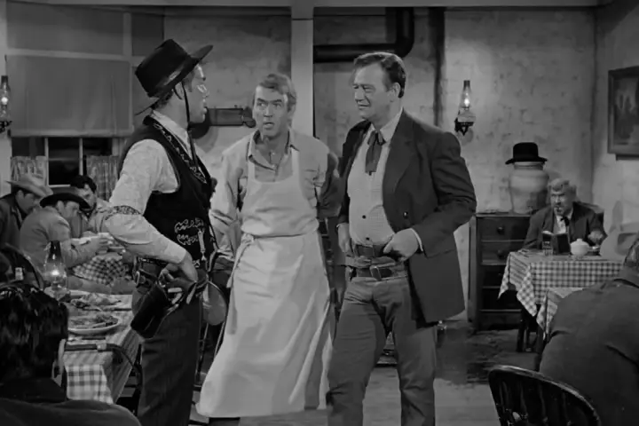 Inquadratura americana di tre uomini in un saloon. Uno indossa un grembiule, gli altri abiti western.