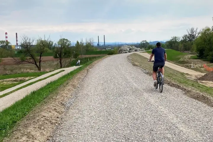 Mężczyzna na rowerze przemierza nową ścieżkę rowerową w Skawinie. W tle widać przemysłowe kominy i zielone tereny.