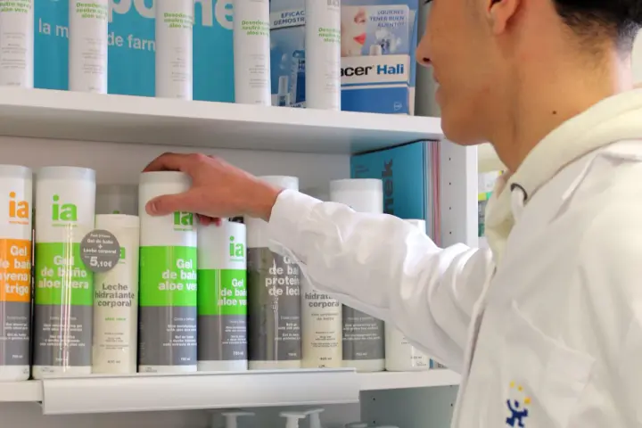 Un técnico superior en farmacia revisa productos en un estante, incluyendo geles de baño y desodorantes.