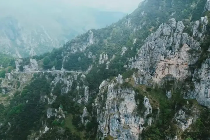 Strada tortuosa che sale verso il passo Barmone, tra rocce imponenti e vegetazione lussureggiante.