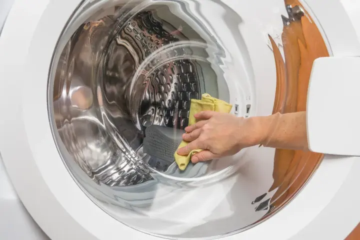 Main d'une personne utilisant un chiffon jaune pour nettoyer l'intérieur d'une machine à laver, une méthode naturelle pour nettoyer machine a laver vinaigre.