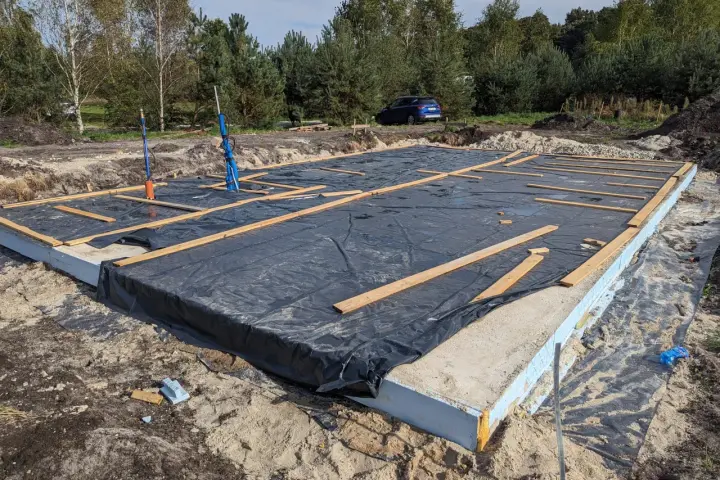 Płyta fundamentowa z folią i drewnianymi elementami na budowie domu szkieletowego.