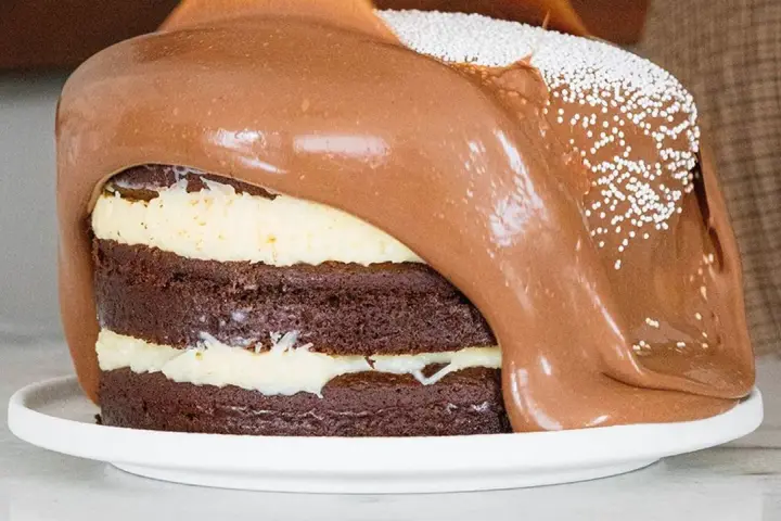 Torta al cioccolato a strati con glassa al cioccolato fusa che cola, decorata con perline bianche. Un vero tsunami di dolcezza!