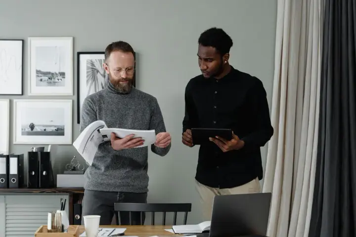Two men review documents and a tablet, discussing the details of in-kind donation accounting.