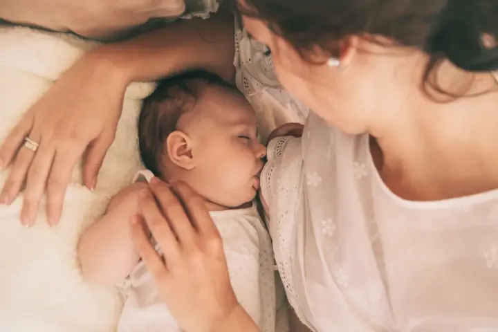 Delikatne karmienie noworodka. Mama czule tuli dziecko, które śpi, ssąc pierś. Wskazówki, jak wybudzić noworodka do karmienia, mogą być pomocne w takich chwilach.