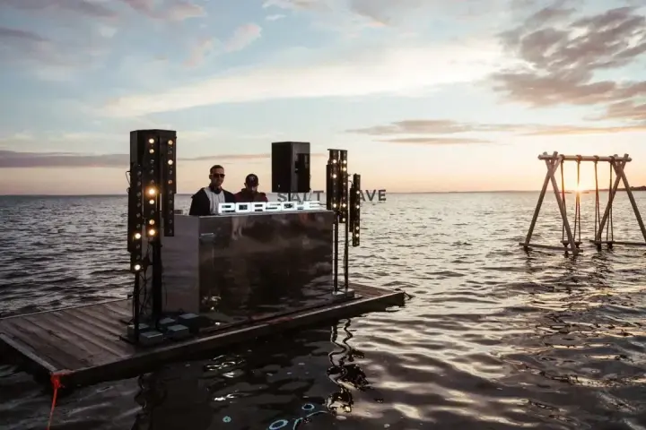 DJ na wodnej platformie podczas Salt Wave Festival. W tle huśtawka na jeziorze o zachodzie słońca.