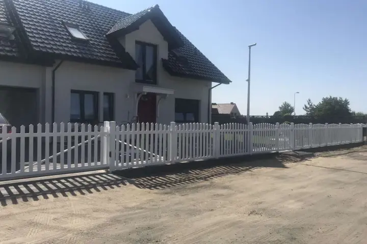 Biały płotek ogrodowy zrób to sam, idealnie otacza dom. Wygląda jak nowy, dodaje uroku posesji.