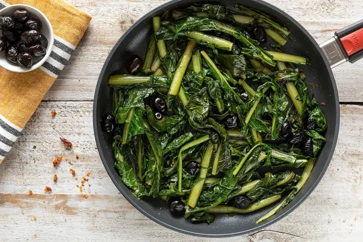 Verdura di catalogna saltata in padella con olive nere. Un piatto semplice e gustoso, pronto per essere servito.