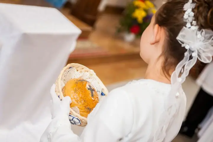 Dziewczynka w bieli trzyma koszyczek z opłatkiem. Zastanawiasz się, ile daje chrzestny na komunię?