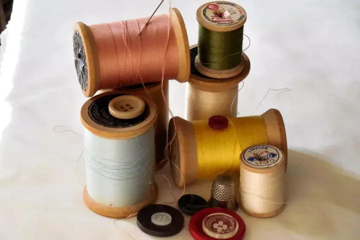Bobine di filo colorato, bottoni e un ditale, pronti per un punto sopraggitto a mano.