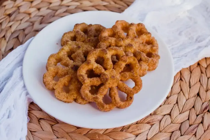 Buñuelos dorados con azúcar y canela en un plato blanco.