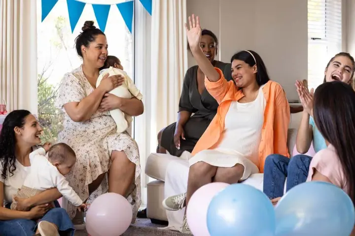 Glada kvinnor firar en babyshower med ballonger och bebisar. En kvinna vinkar glatt.
