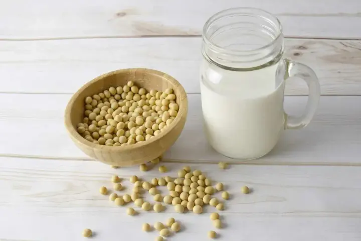 Misternie ułożone ziarna soi w drewnianej misce i szklanka mleka sojowego. Czy soja ma gluten? Nie, soja jest bezglutenowa.