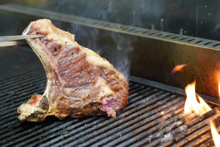 Una succulenta bistecca alla fiorentina, con la sua storia di sapori, cuoce sulla griglia tra fiamme vive e fumo.