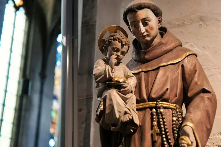 A statue shows what friars wear: brown robes, a cord belt, and a rosary. A child with a halo holds fruit.