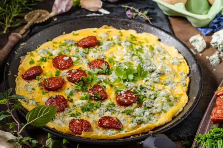 Pyszny omlet na słono z kawałkami chorizo i niebieskim serem, posypany szczypiorkiem i natką pietruszki.