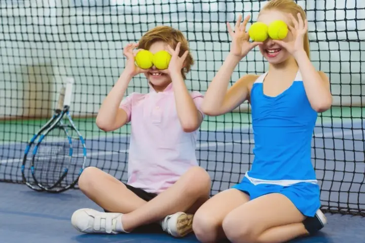 Bambini che fanno sport, con palline da tennis sugli occhi, ridono su un campo da tennis.