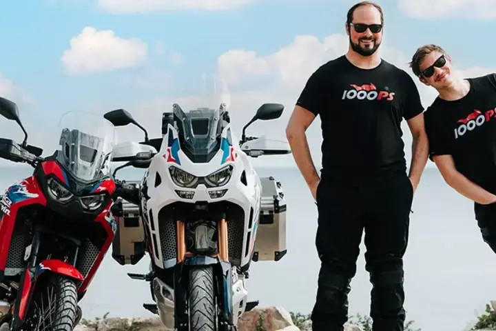 Dwóch mężczyzn w koszulkach 1000PS obok motocykli Honda Africa Twin.