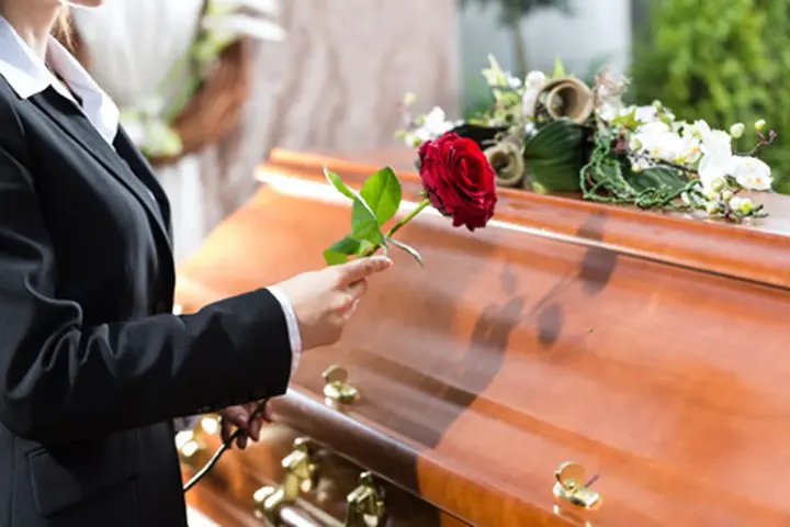 Eine Frau in Trauer legt eine rote Rose auf den Sarg. Sie muss die Beerdigung ihres getrennt lebenden Ehemanns bezahlen.